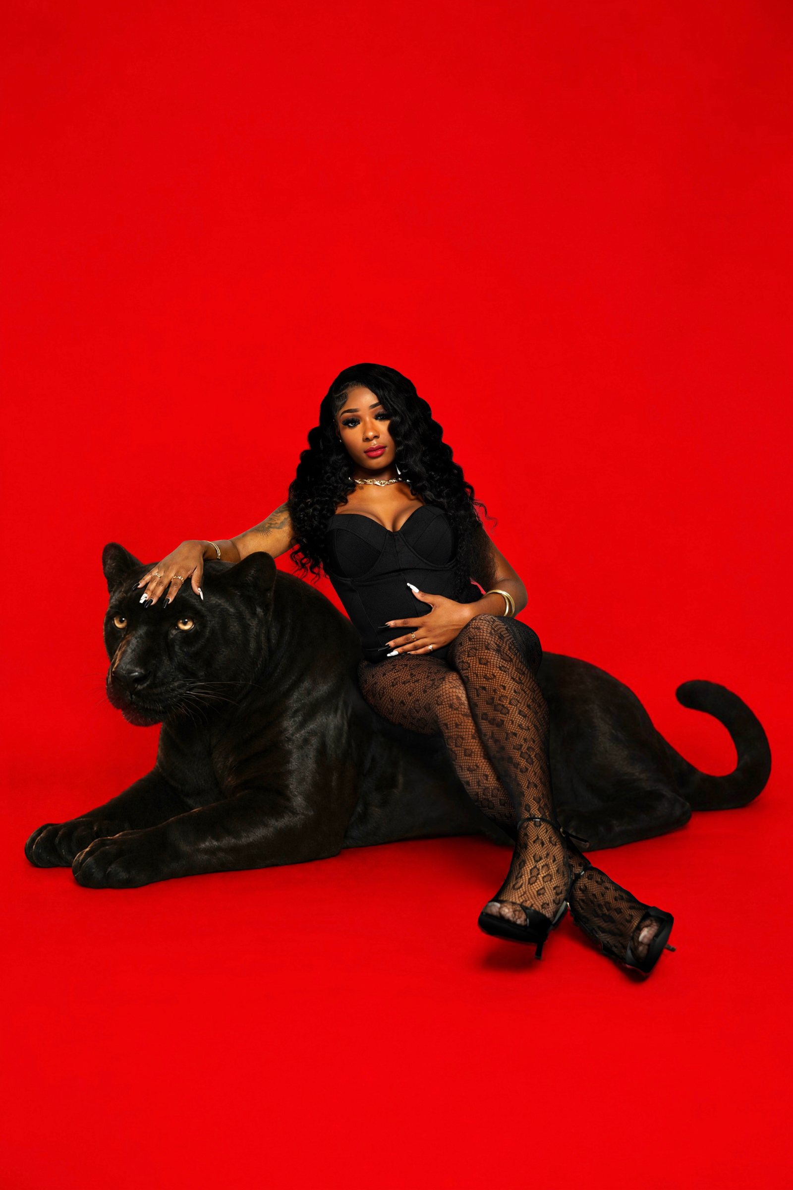 A single woman styled in a black bustier and fishnets posed on the black panther prop against the saturated red seamless
